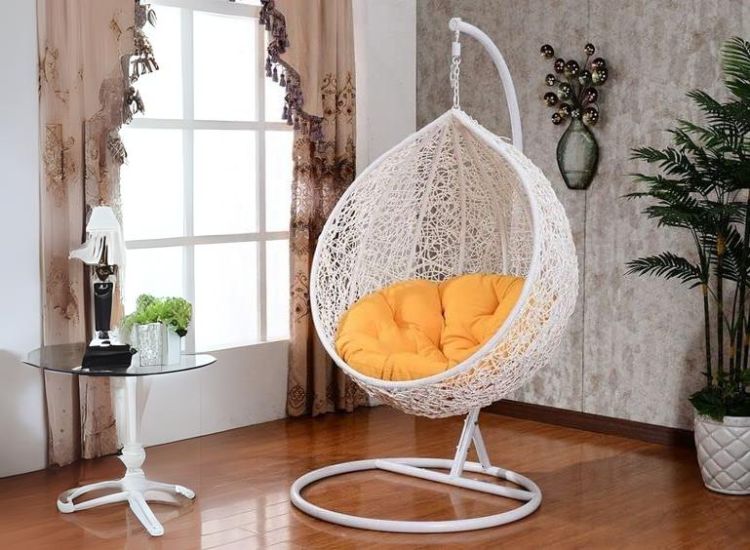 Single-seated swing with a white stand, adorned with yellow cushions, placed beside a window in a cozy living room setting.