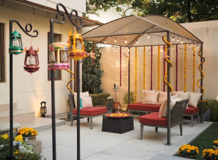 A charming outdoor area featuring a small gazebo with seating chairs, adorned with fairy lights, garlands, and lanterns hanging from the poles.